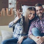 Una coppia felice che ha attorno scatole per il trasloco ed una scritta sulla sinistra fatta in mattoni "IMU"