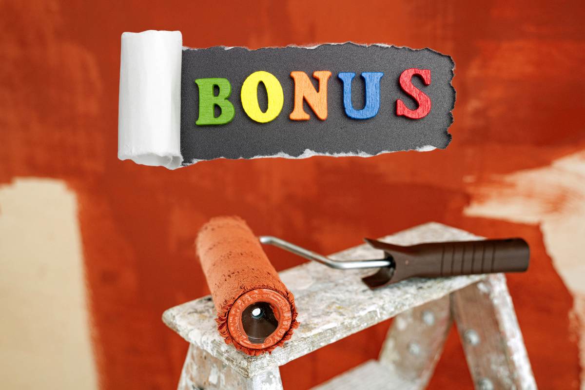 Un rullo per tinteggiare colorato di rosso ed un muro sullo sfondo tinteggaito di rosso e con sopra una scritta "bonus"