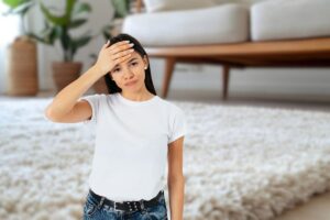 donna con mano sulla fronte in primo piano e soggiorno in cui si vede un tappeto