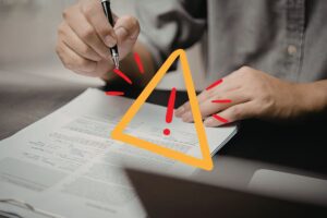 Una persona che firma un contratto ed un segnale di pericolo in primo piano