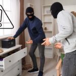 Dei ladri che stanno derubando una casa ed un segnale di pericolo in alto a sinistra