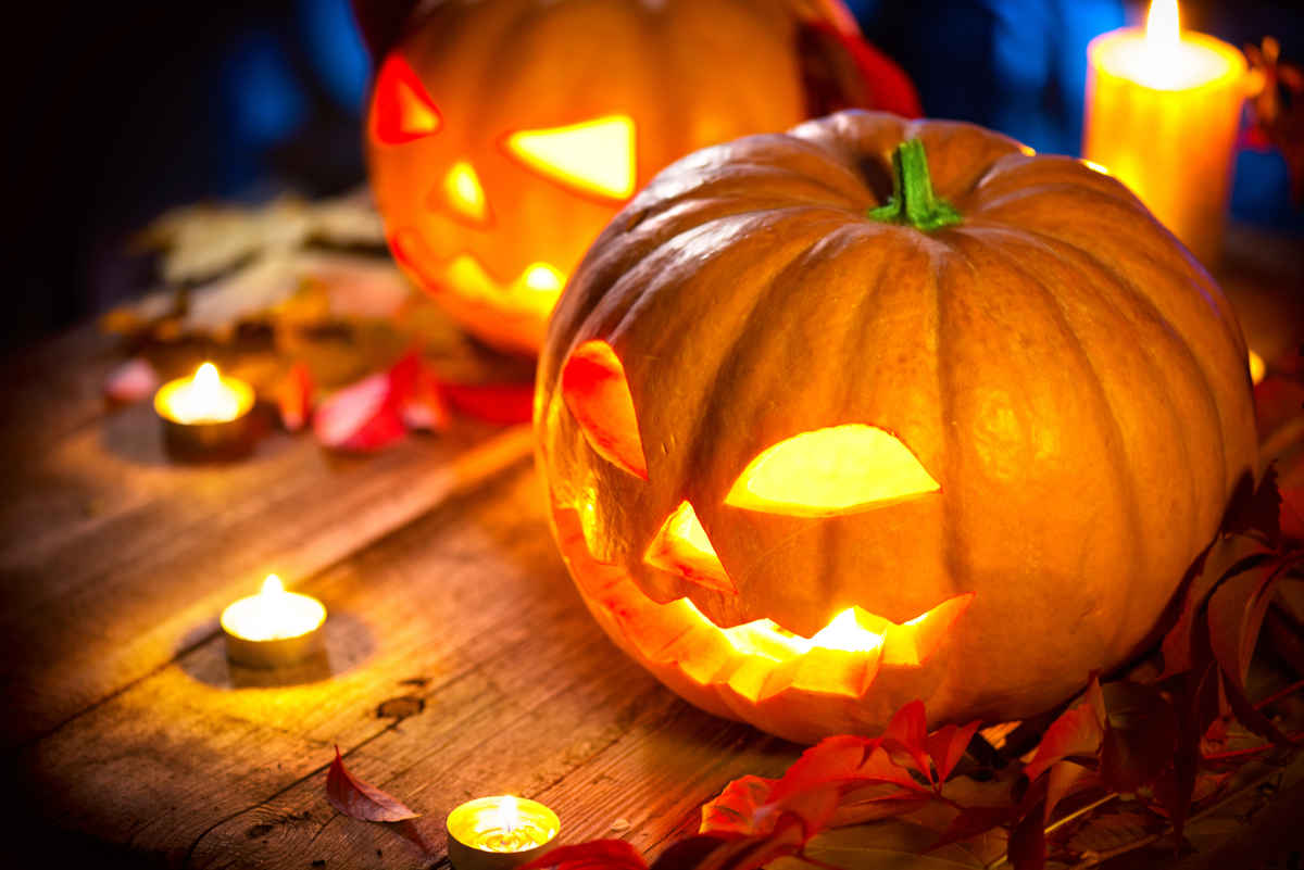 zucca di halloween illuminata con candele intorno poggiate su un tavolo di legno
